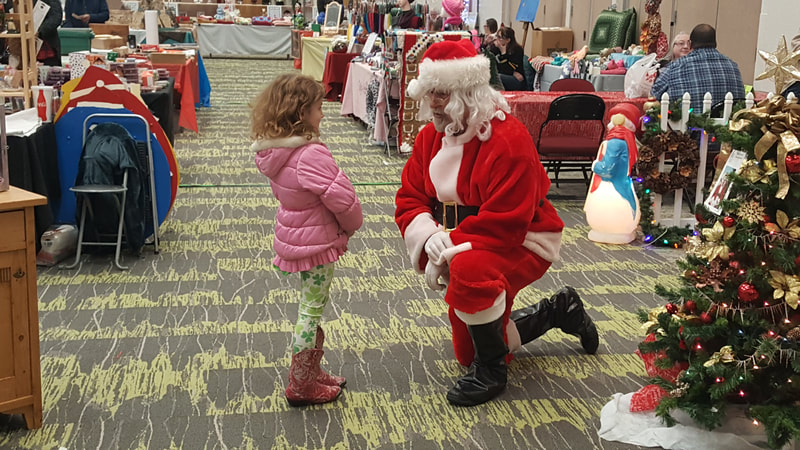 Santa kneeling in front of little girl with curly blonde hair and pink jacket smiling